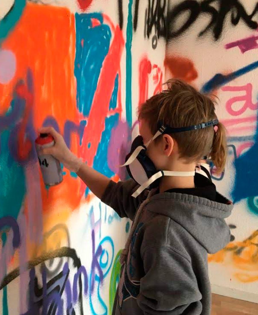 Kind mit Atemschutzmaske sprüht ein Graffiti an die Wand