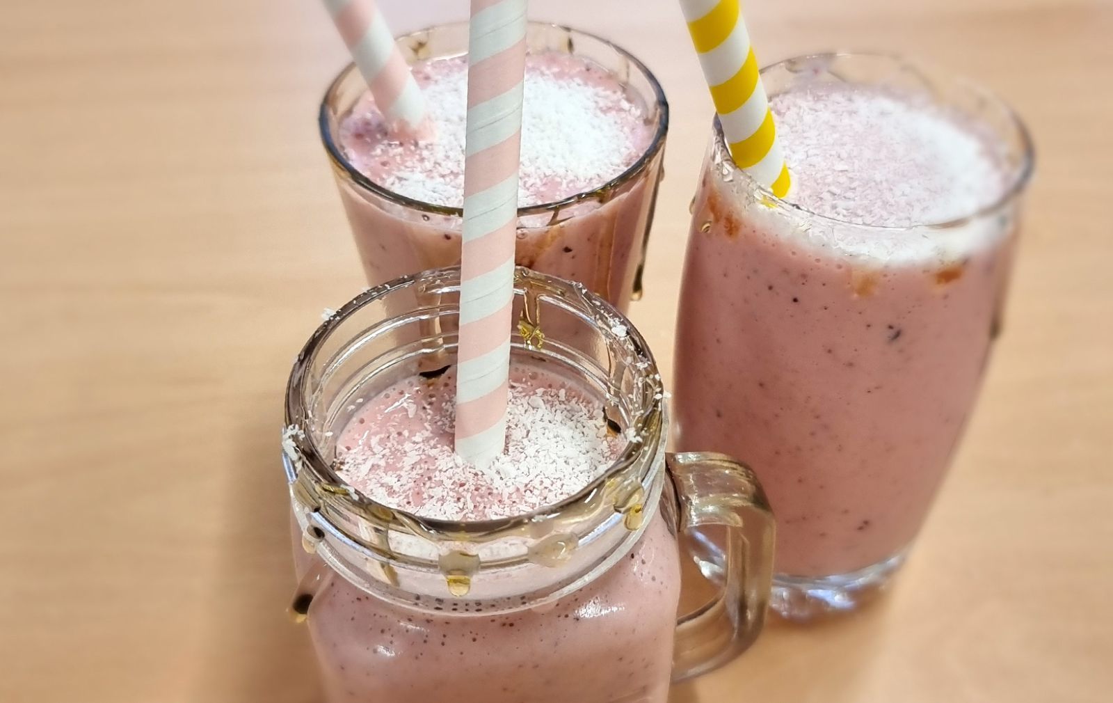 drei Erdbeermilchskaes im Glas mit Strohalm auf einer Tischplatte