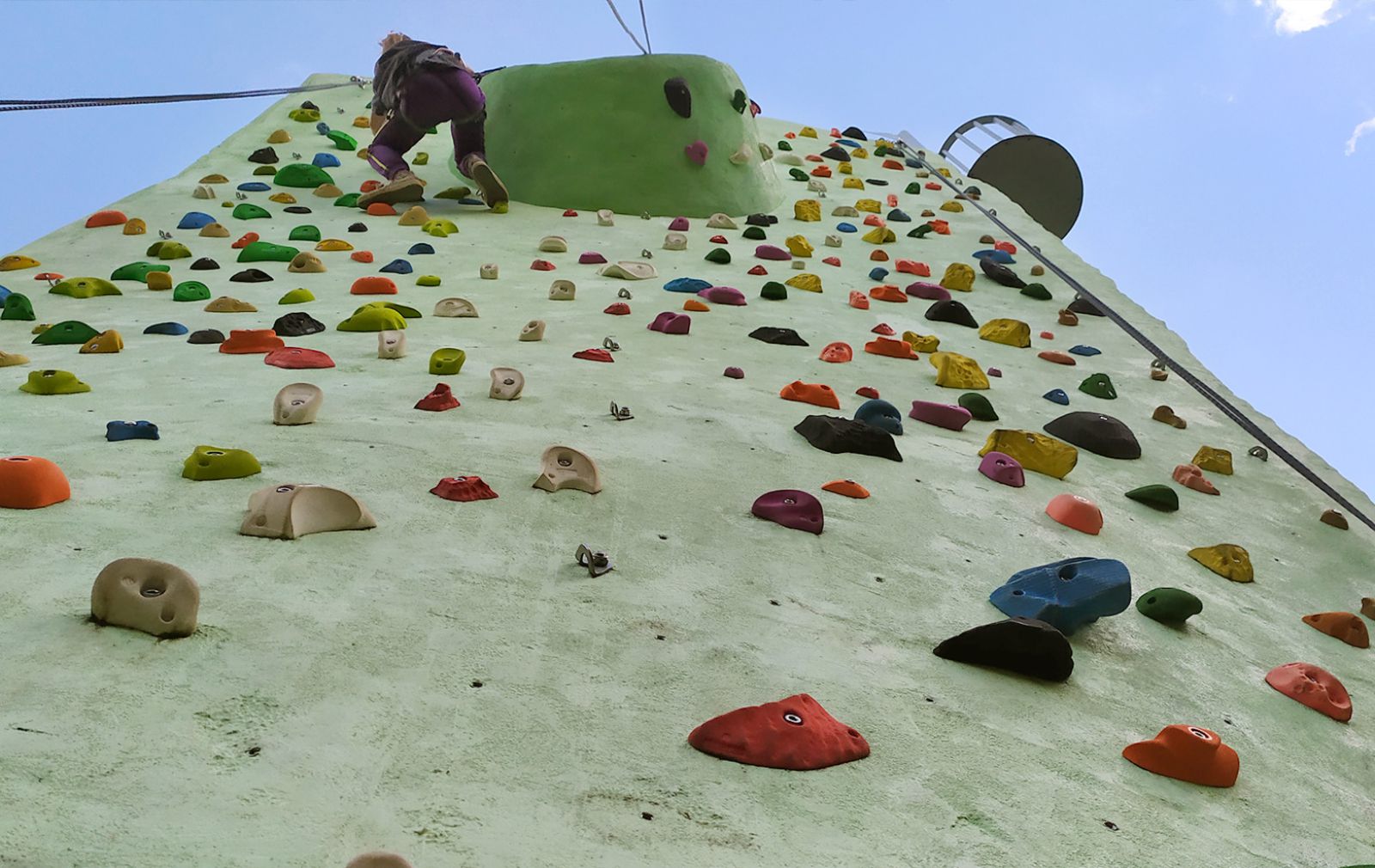 Ansicht von unten wie ein Jugendlicher den Kletterfelsen erklimmt