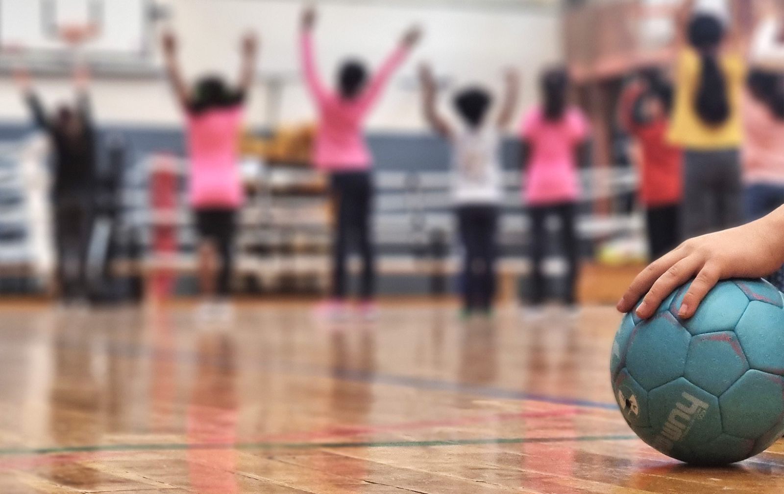 Kinder mit hocherhobenen Armen, ein Ball im Vordergrund